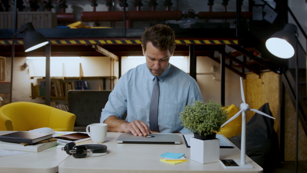 Mature man with laptop sitting indoors at desk in home office, working.