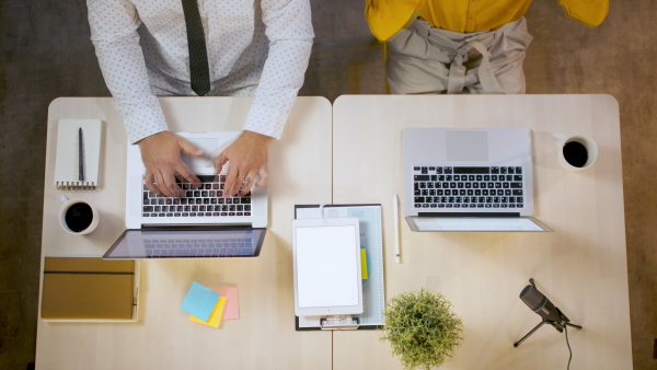 Timelapse top shot of unrecognizable man and woman sitting indoors at desk in office, working with laptop.