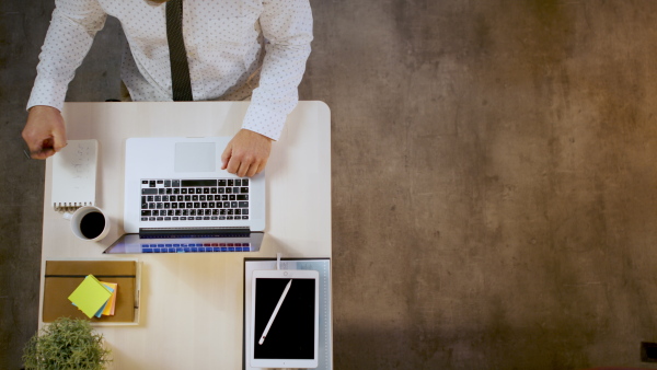 Top view of unrecognizable man sitting indoors at desk in office, working with laptop.