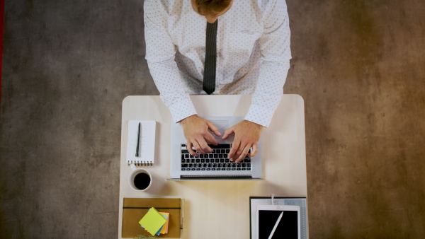 Top view of unrecognizable man sitting indoors at desk in office, working with laptop.