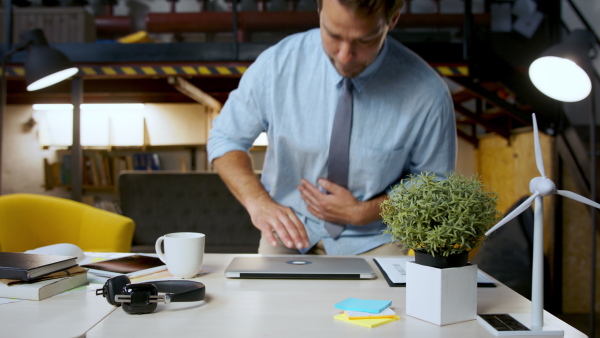 Mature man with laptop sitting indoors at desk in home office, working.