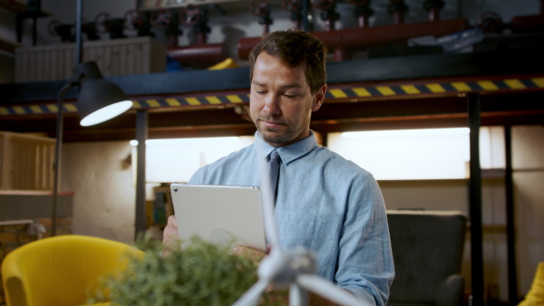 Mature man with tablet sitting indoors at desk in home office, working.