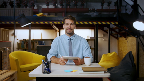 Mature man with tablet sitting indoors at desk in home office, working.