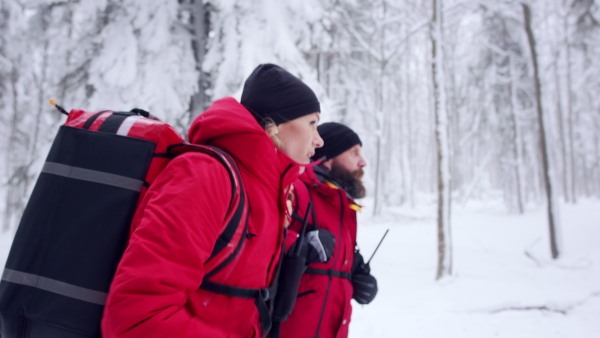 Side view of man and woman paramedics from mountain rescue service running outdoors in winter in forest.