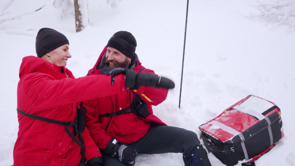 Mountain rescue service on operation outdoors in winter in forest, celebrating.