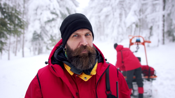 A man paramedic from mountain rescue service outdoors in winter in forest, looking at camera.