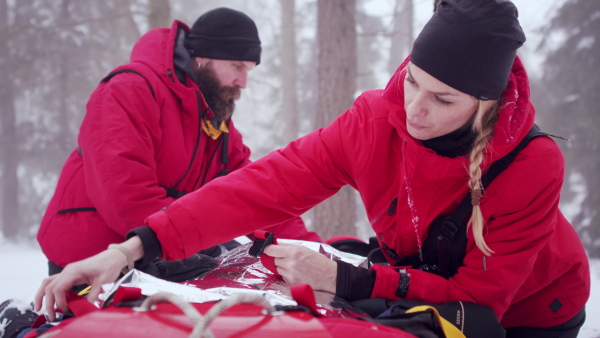 Paramedics from mountain rescue service provide operation outdoors in winter in forest, injured person in stretcher.