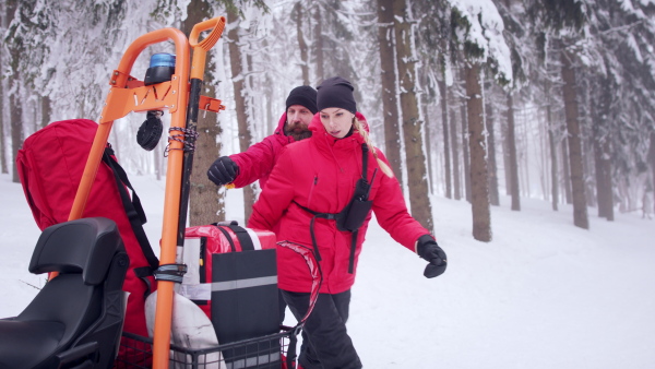 Man and woman paramedics from mountain rescue service provide operation outdoors in winter in forest.