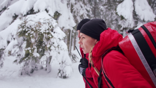 Side view of man and woman paramedics from mountain rescue service running outdoors in winter in forest.