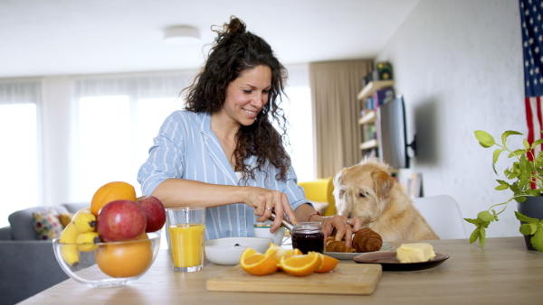 Portrait of woman with pet dog preparing breakfast indoors at home.