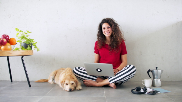 Portrait of woman with pet dog indoors at home, using laptop.