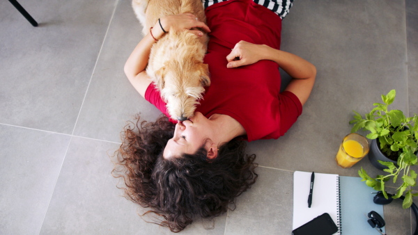 Top view of happy woman with pet dog lying indoors at home, relaxing.