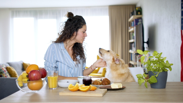 Happy woman with pet dog eating breakfast indoors at home.