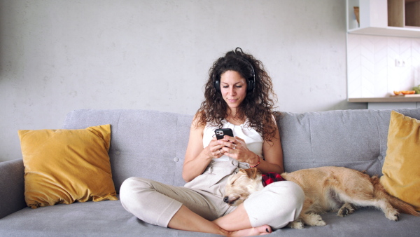 Woman with pet dog and smartphone sitting indoors at home, using smartpbone.