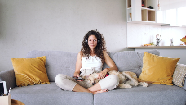 Relaxed woman with two pet dogs sitting indoors at home, listening to music.