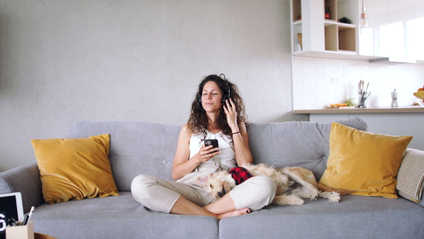 Relaxed woman with two pet dogs sitting indoors at home, listening to music.