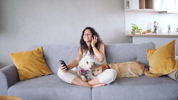 Relaxed woman with two pet dogs sitting indoors at home, listening to music.