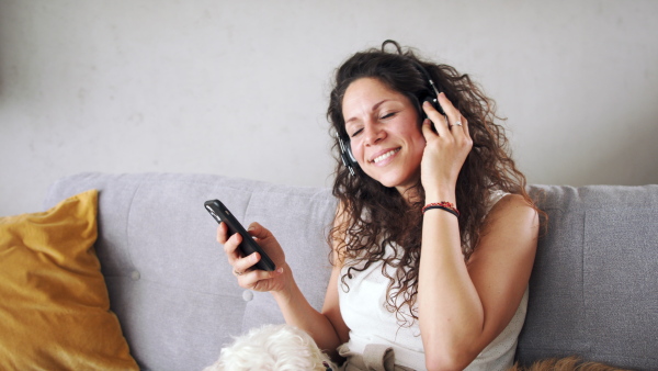 Relaxed woman with two pet dogs sitting indoors at home, listening to music.