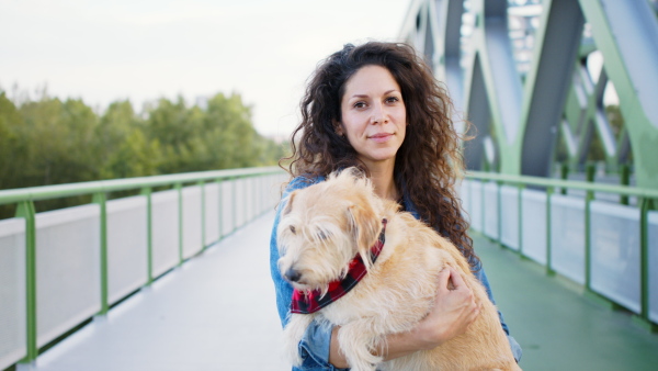 Front view of woman with pet dog standing outdoors in city, looking at camera.