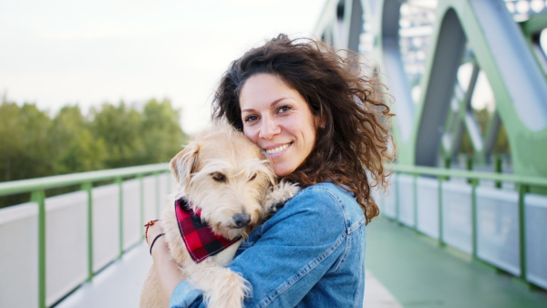 Front view of woman with pet dog standing outdoors in city, looking at camera.