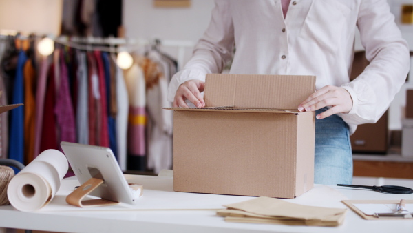 Unrecognizable young woman dropshipper with tablet working at home, coronavirus concept.