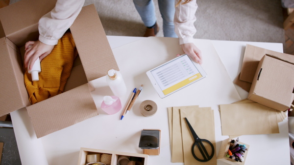 Unrecognizable young woman dropshipper working at home, using tablet. Coronavirus concept.