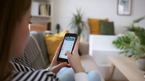 Rear view of young woman with smartphone ordering food at home, coronavirus and food delivery concept.