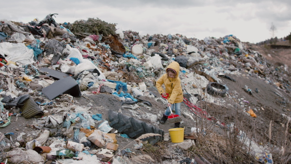 Small child with bucket and spade playing on landfill, environmental pollution concept.