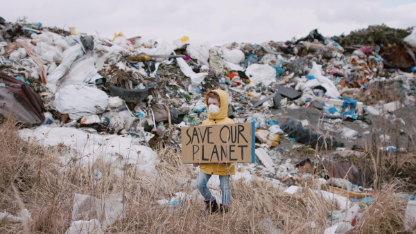 Front view of small child holding placard poster on landfill, environmental pollution concept.