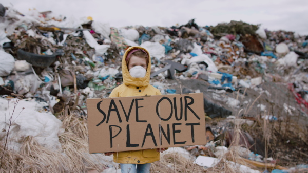 Front view of small child holding placard poster on landfill, environmental pollution concept.