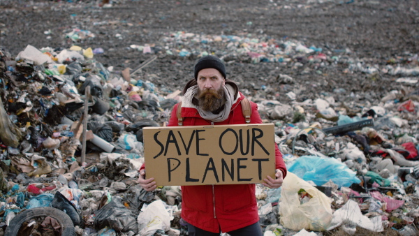 Front view of man activist holding placard poster on landfill, environmental pollution concept.