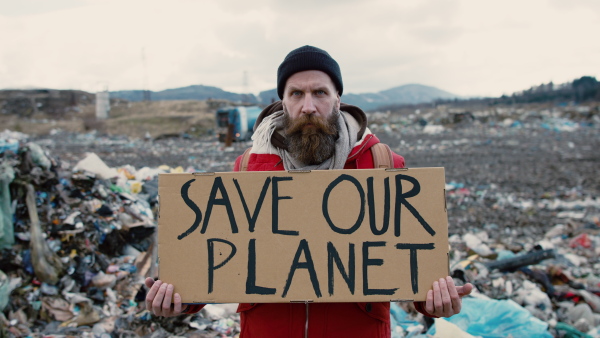 Front view of man activist holding placard poster on landfill, environmental pollution concept.