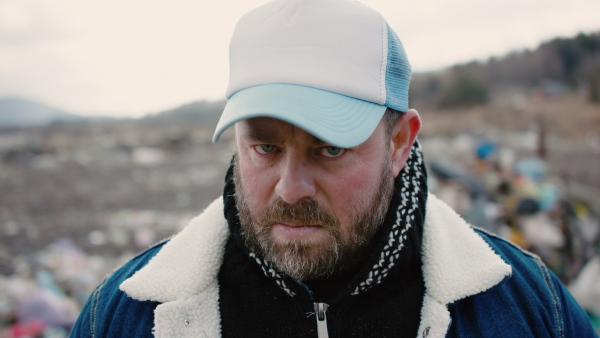 Man activist standing on landfill and looking at camera, environmental pollution concept.