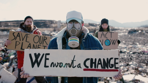 Group of activists with gas mask and placard posters on landfill, environmental pollution concept.