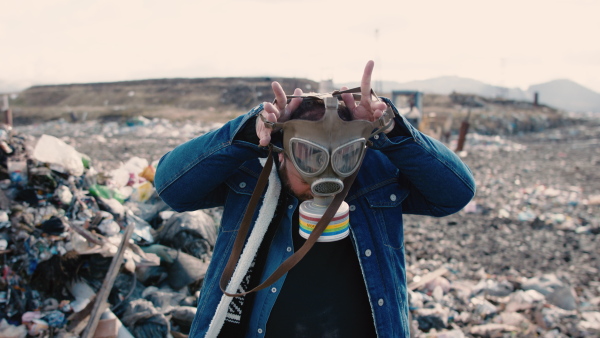 Front view of man putting on gas mask on landfill, environmental concept. Slow motion.