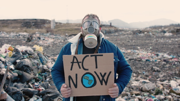 Front view of man with gas mask and placard poster on landfill, environmental concept.