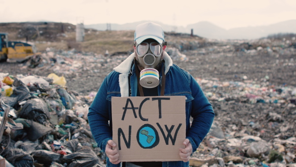 Front view of man with gas mask and placard poster on landfill, environmental concept.