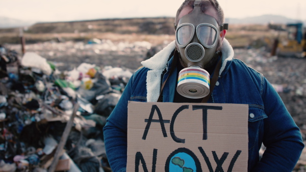 Front view of man with gas mask and placard poster on landfill, environmental concept.