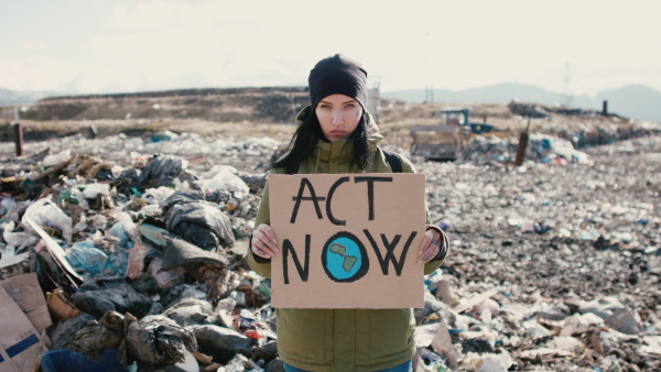 Woman activist holding placard poster on landfill, environmental pollution concept.