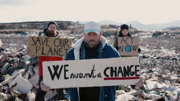 Group of activists with placard posters looking at camera on landfill, environmental pollution concept.