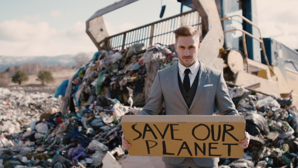 Modern businessman with placard poster on landfill, consumerism versus pollution concept.