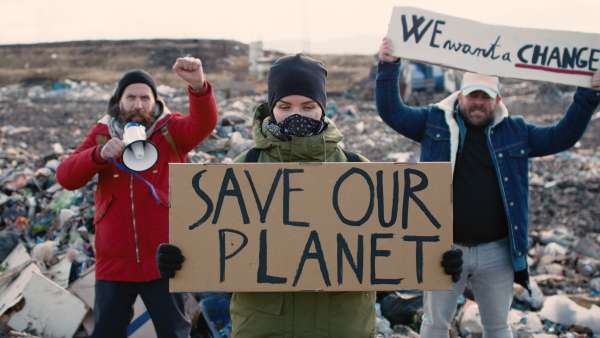 Group of activists with placard posters looking at camera on landfill, environmental pollution concept.