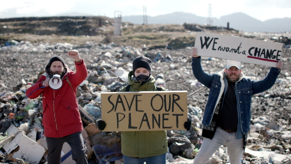 Group of activists with placard posters looking at camera on landfill, environmental pollution concept.