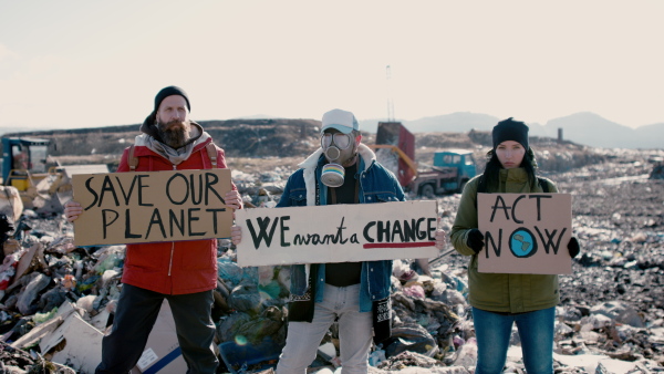 Group of activists with gas mask and placard posters on landfill, environmental pollution concept.