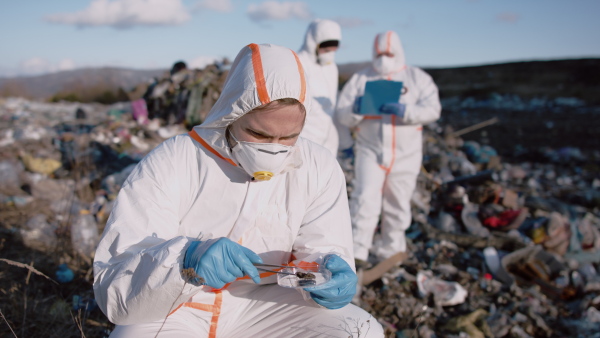 Group of activists or scientists with protective masks and suits on landfill, environmental pollution concept.