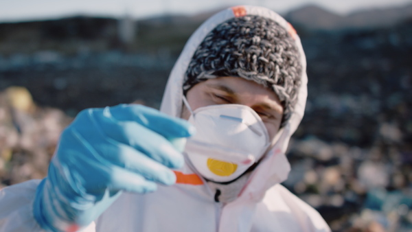 Activist scientist with protective masks holding tube with sample on landfill, environmental pollution concept.