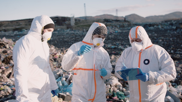 Group of activists or scientists with protective masks and suits on landfill, environmental pollution concept.