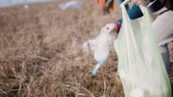 Close-up midsection of man activist picking up litter in nature, environmental pollution concept.