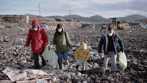 Group of activists with face masks walking on landfill, environmental pollution concept.