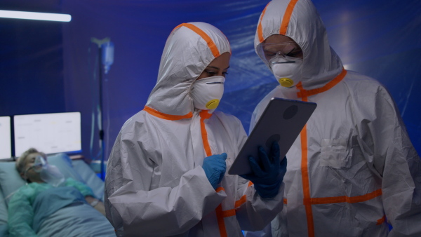 Doctors with protective suits and tablet talking in hospital, coronavirus concept.